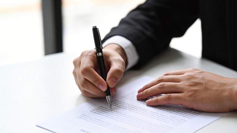 身穿西装的人正在白色桌面上签署文件图片
