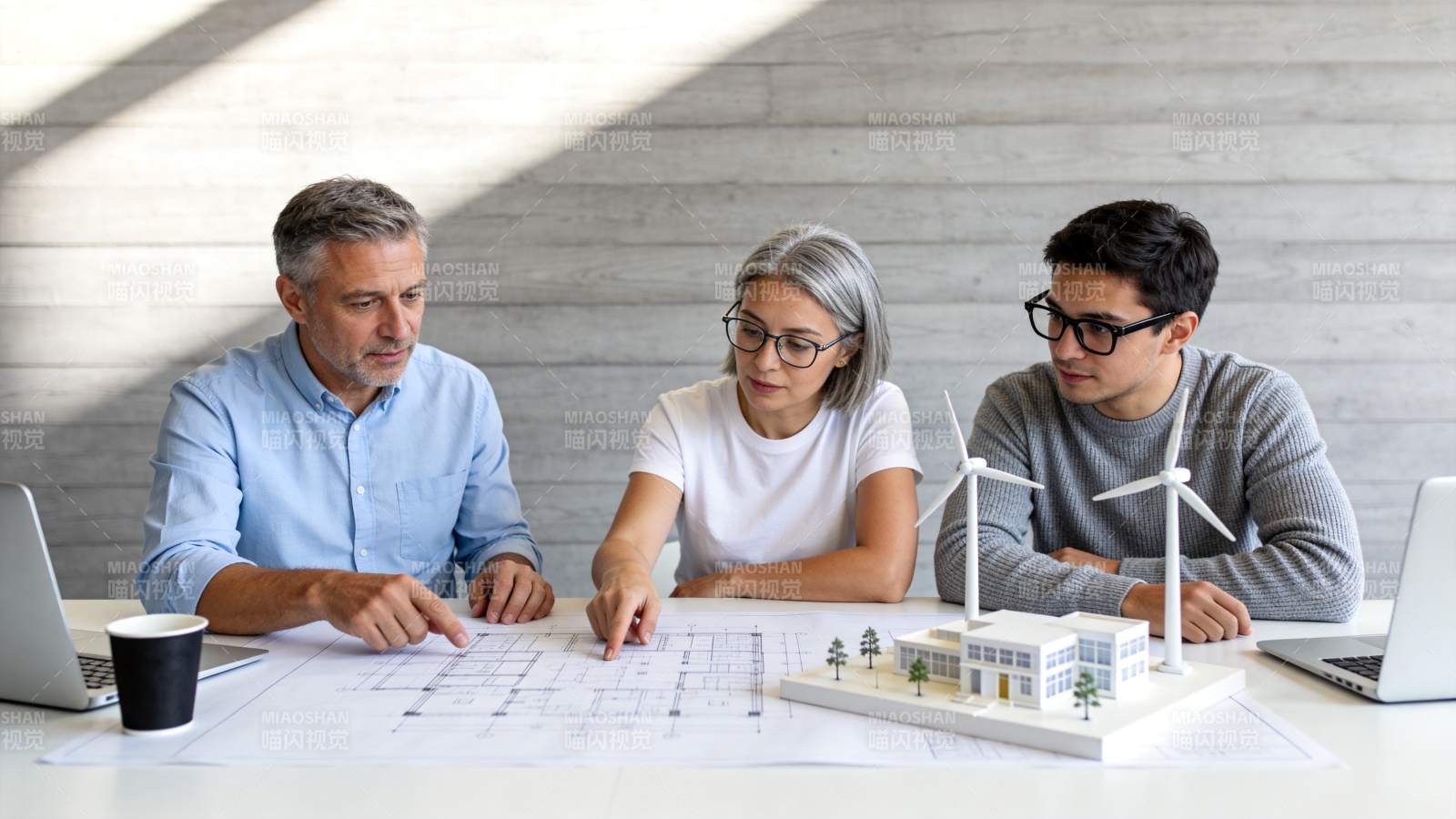 三人围桌讨论建筑图纸与风能模型方案图片