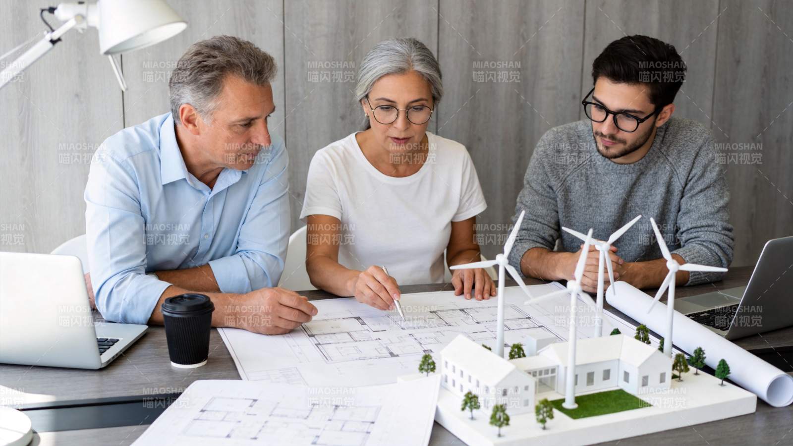 三人围桌讨论建筑模型与图纸方案图片