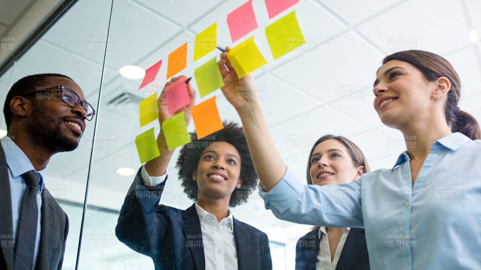 四位职场人员在玻璃墙贴彩色便签讨论工作图片