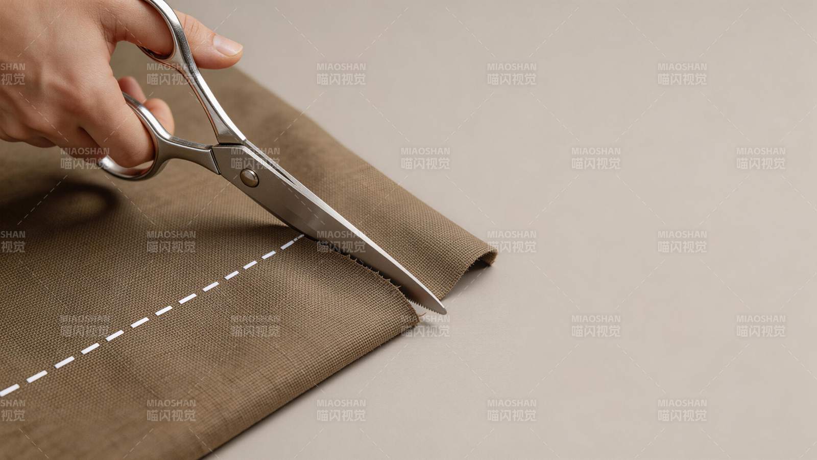 手持剪刀沿虚线裁剪棕色布料的特写画面图片