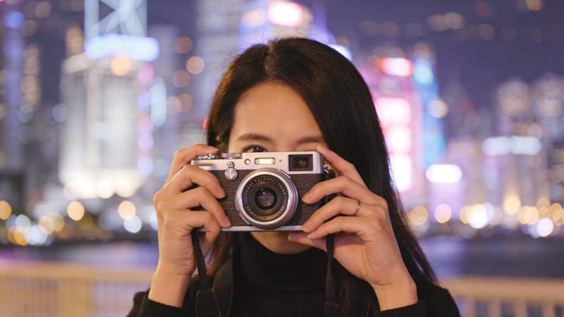 女子手持复古相机拍摄夜景城市灯光图片