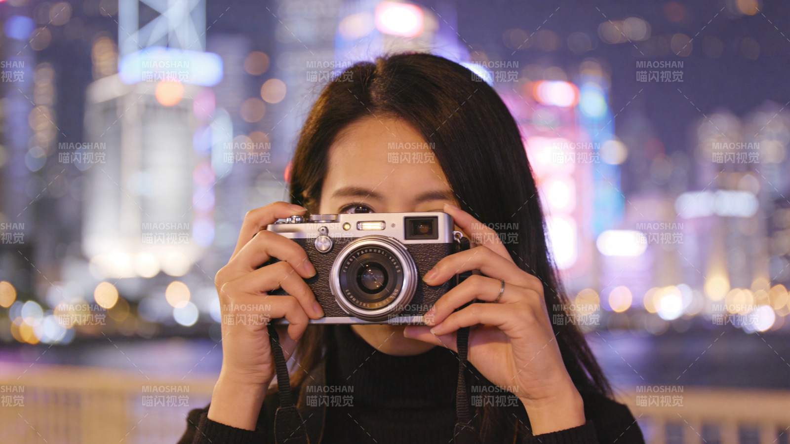 女子手持复古相机拍摄夜景城市灯光图片