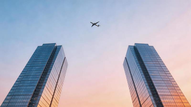 双塔高楼间飞行客机与渐变天空图片