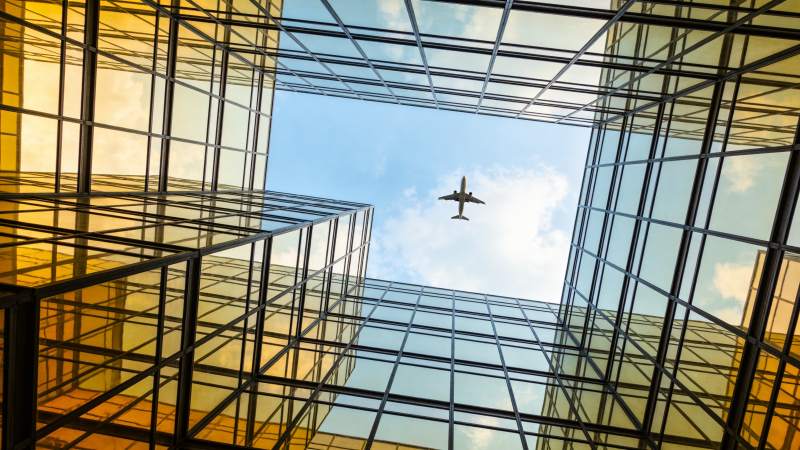 玻璃幕墙高楼间飞行的客机仰视图图片