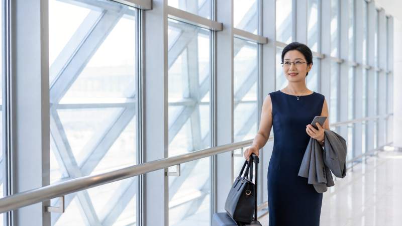穿深蓝连衣裙女子手持手机拉行李箱行走图片