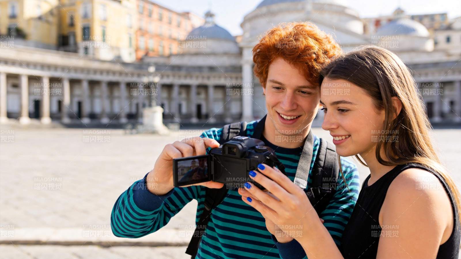 红发青年与同伴在广场用相机查看照片图片