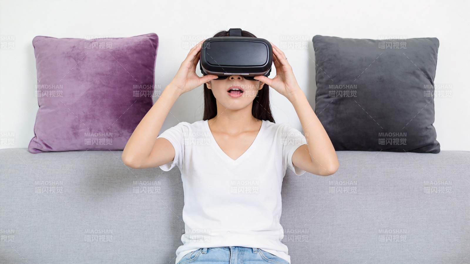 女子佩戴VR眼镜坐在灰色沙发上体验虚拟现图片