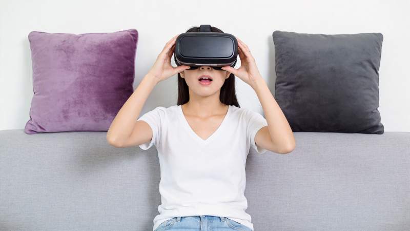 女子佩戴VR眼镜坐在灰色沙发上体验虚拟现图片