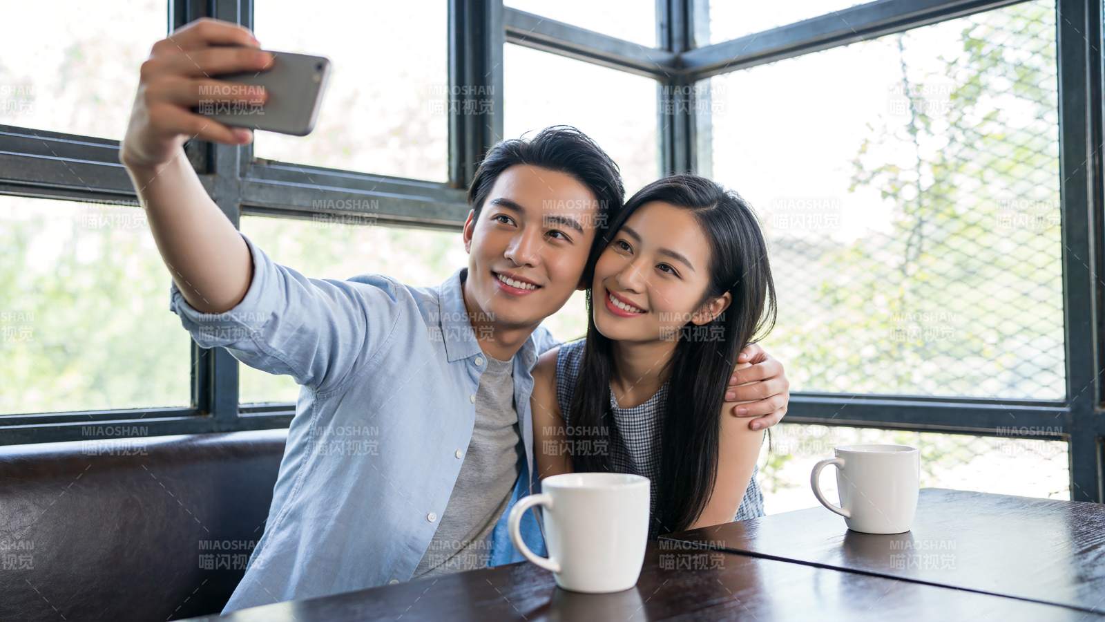 男女在咖啡馆窗边用手机自拍合影图片