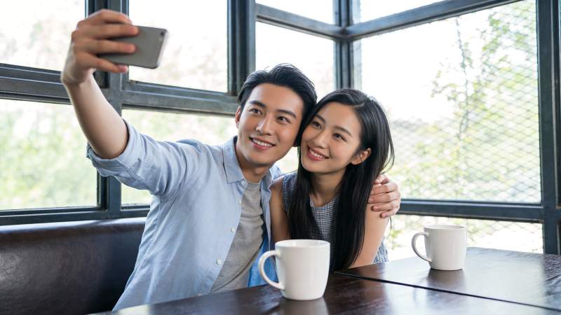 男女在咖啡馆窗边用手机自拍合影图片