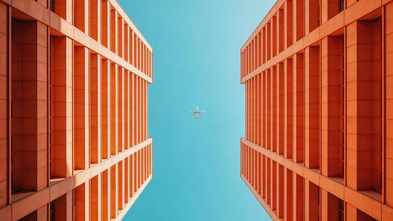 两栋橙色高楼间飞行的客机仰视图图片