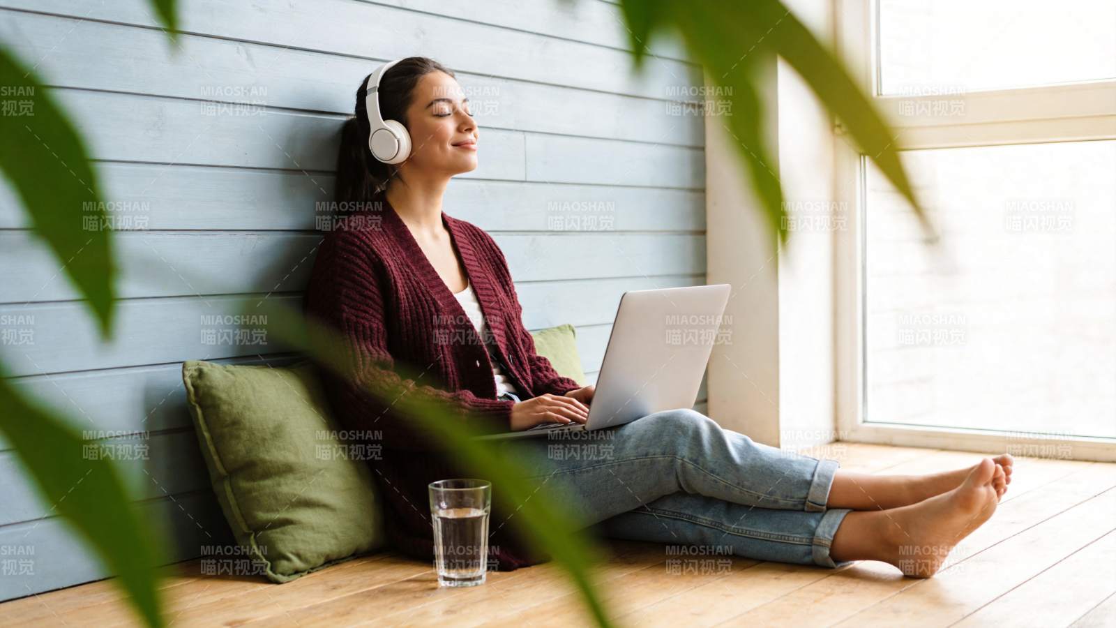 女子戴耳机用笔记本电脑坐在窗边休息图片