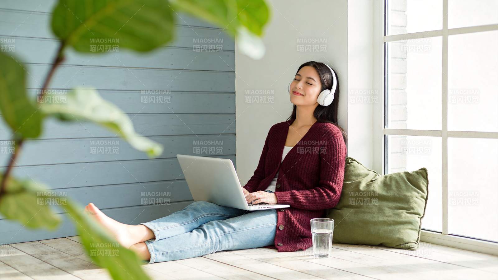 女子戴耳机用笔记本电脑坐在窗边地板图片