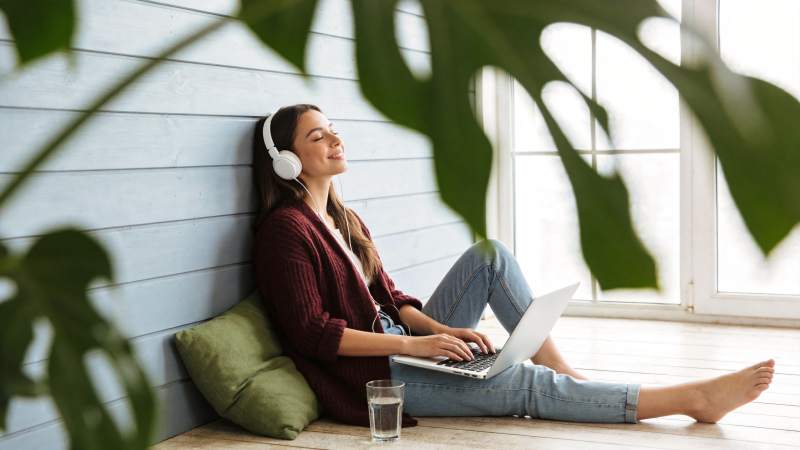 女子戴耳机用笔记本电脑倚墙休息图片