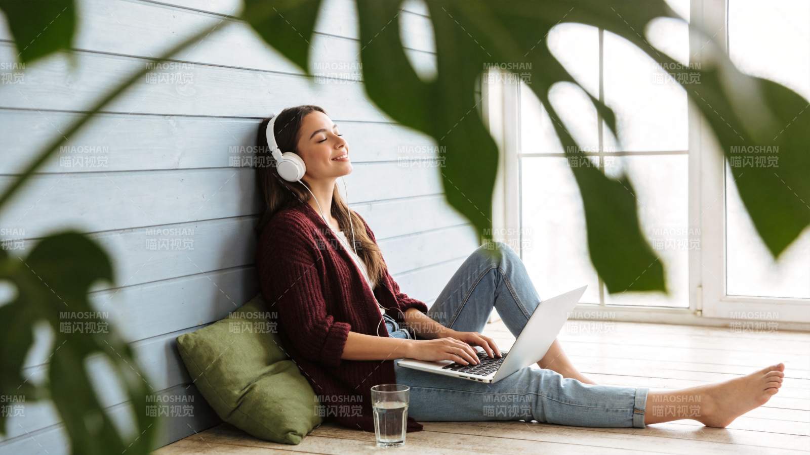 女子戴耳机用笔记本电脑倚墙休息图片