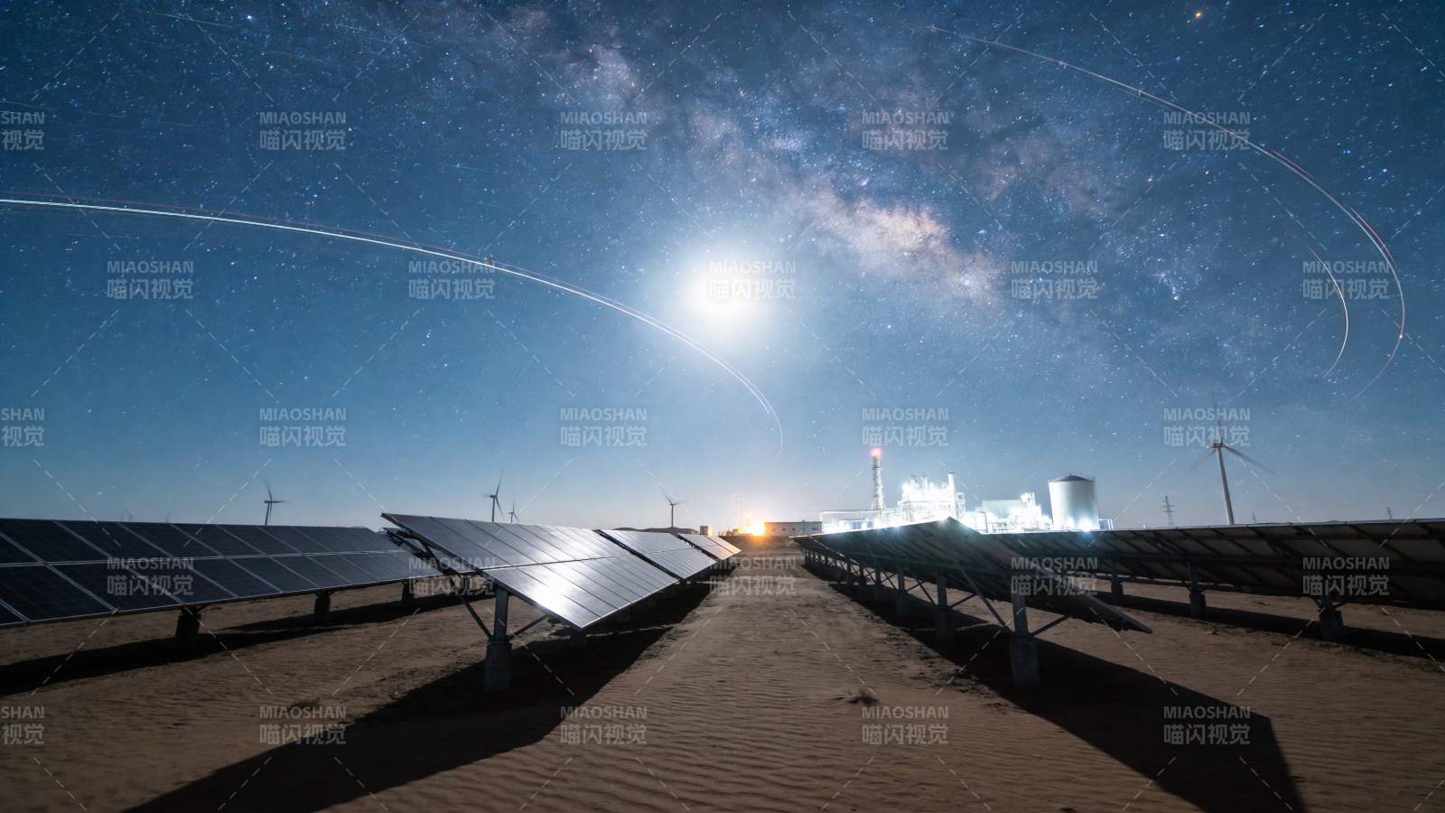 沙漠中太阳能板阵列与星空下的风力发电机图片