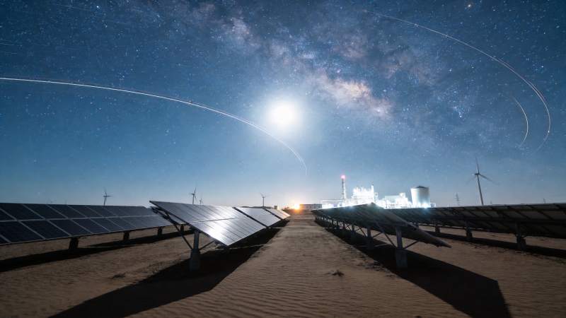 沙漠中太阳能板阵列与星空下的风力发电机图片