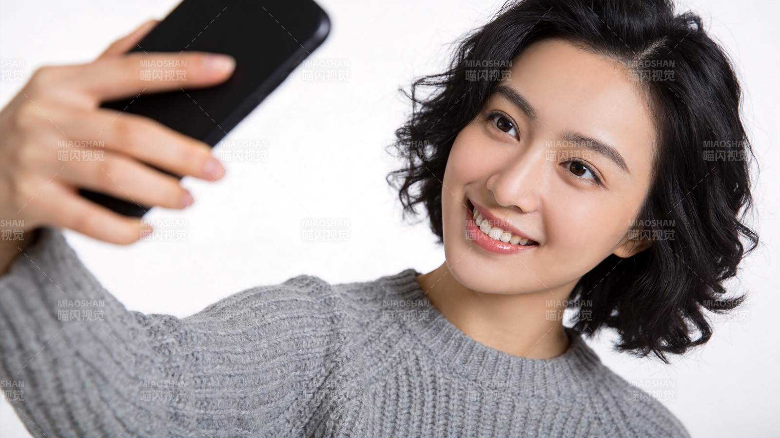 短发女性手持黑色手机自拍微笑图片