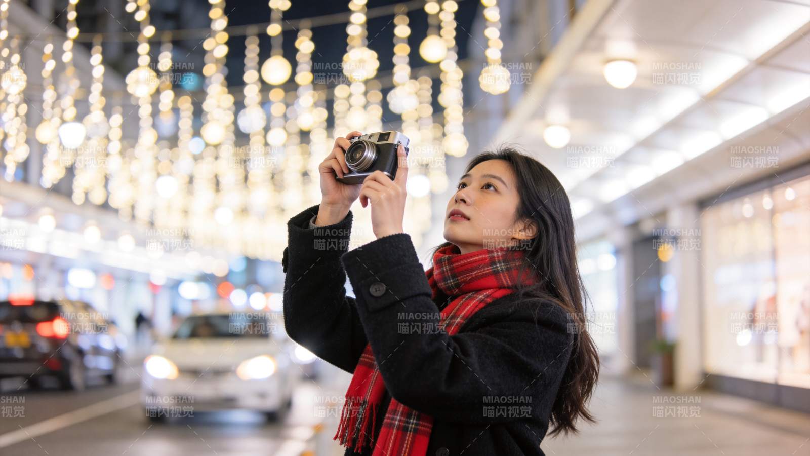 女子手持相机拍摄街景灯光装饰图片