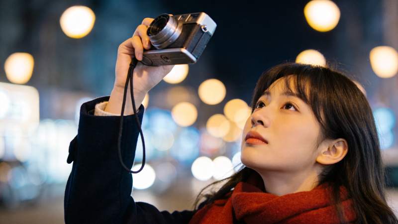 女子夜间手持胶片相机仰拍街景图片