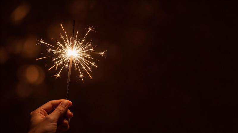 手持点燃的烟花棒在暗色背景中闪烁图片