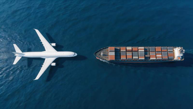 飞机与货轮在蓝色海面上并行航行图片