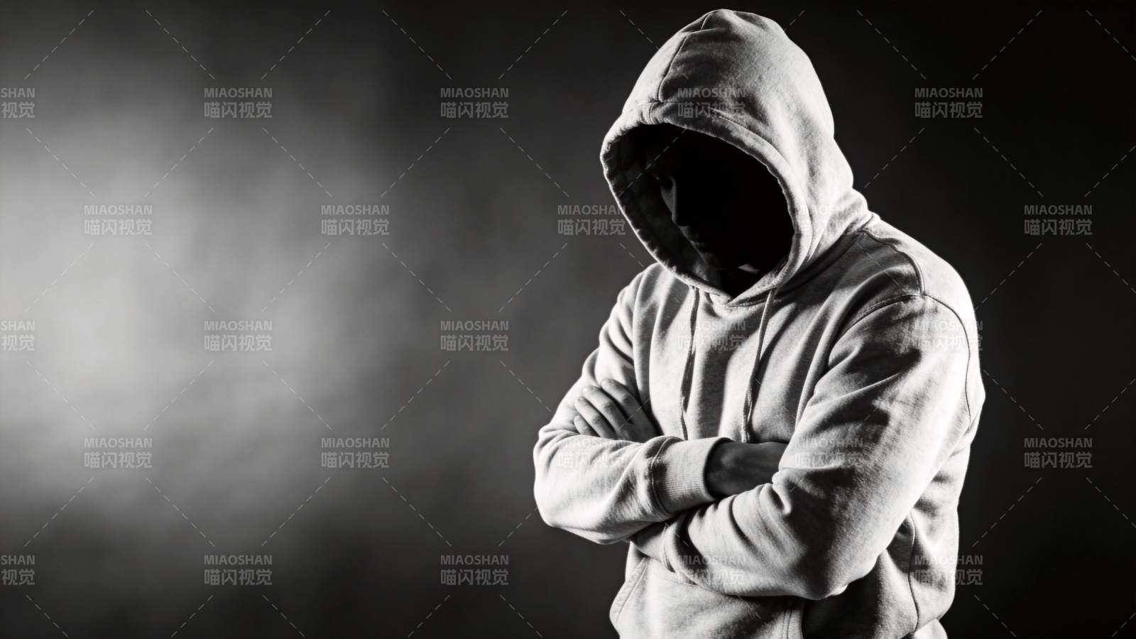 戴兜帽人物双臂交叉站立于暗影背景中图片