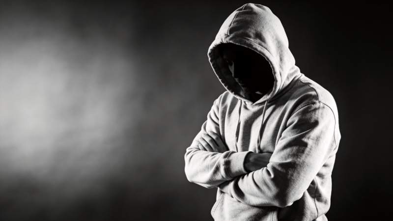 戴兜帽人物双臂交叉站立于暗影背景中图片