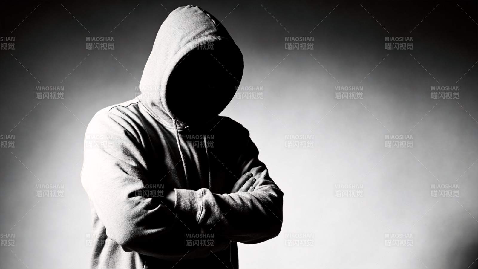 戴兜帽人物双臂交叉站立于暗调背景前图片