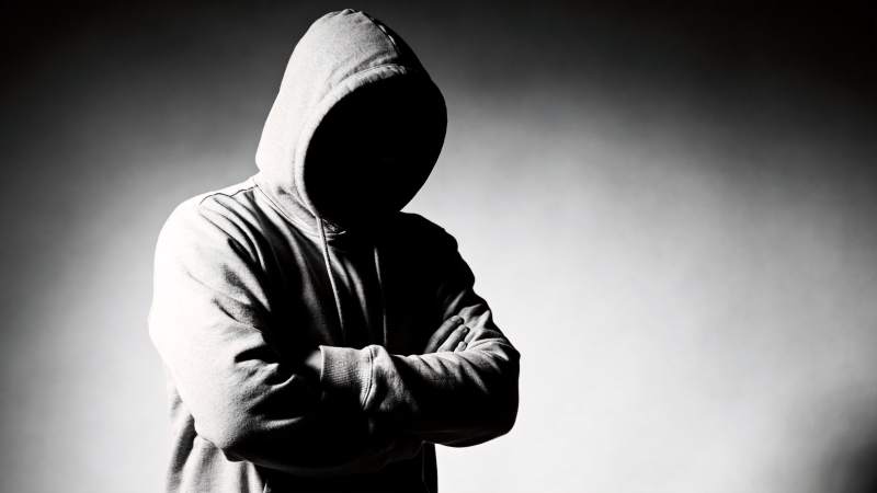 戴兜帽人物双臂交叉站立于暗调背景前图片