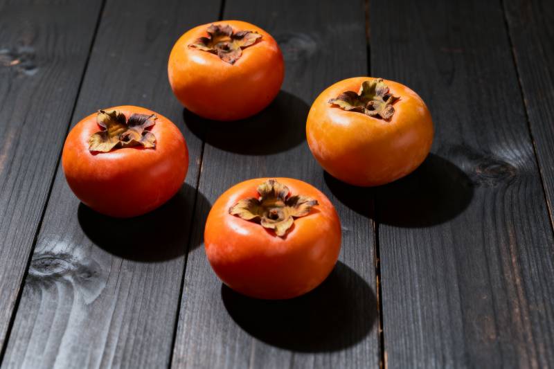 四颗柿子静置于木桌图片