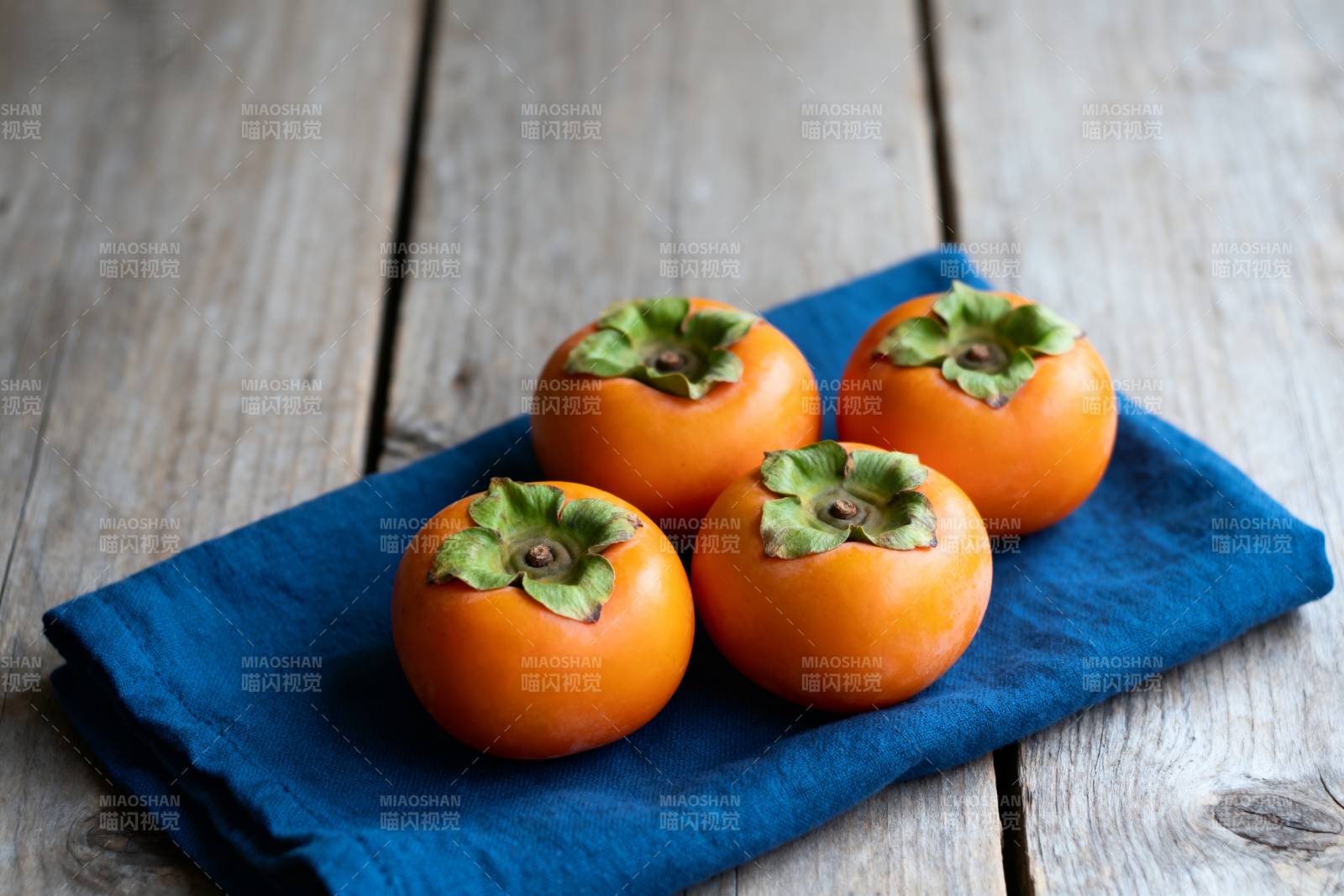 四颗柿子静置于蓝布图片