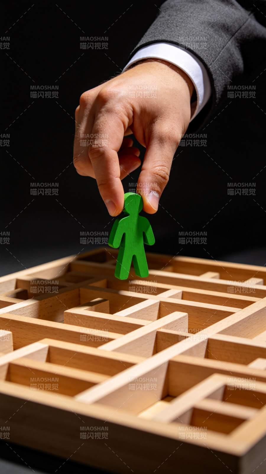 西装手握绿色人形棋子置于木质迷宫上方图片