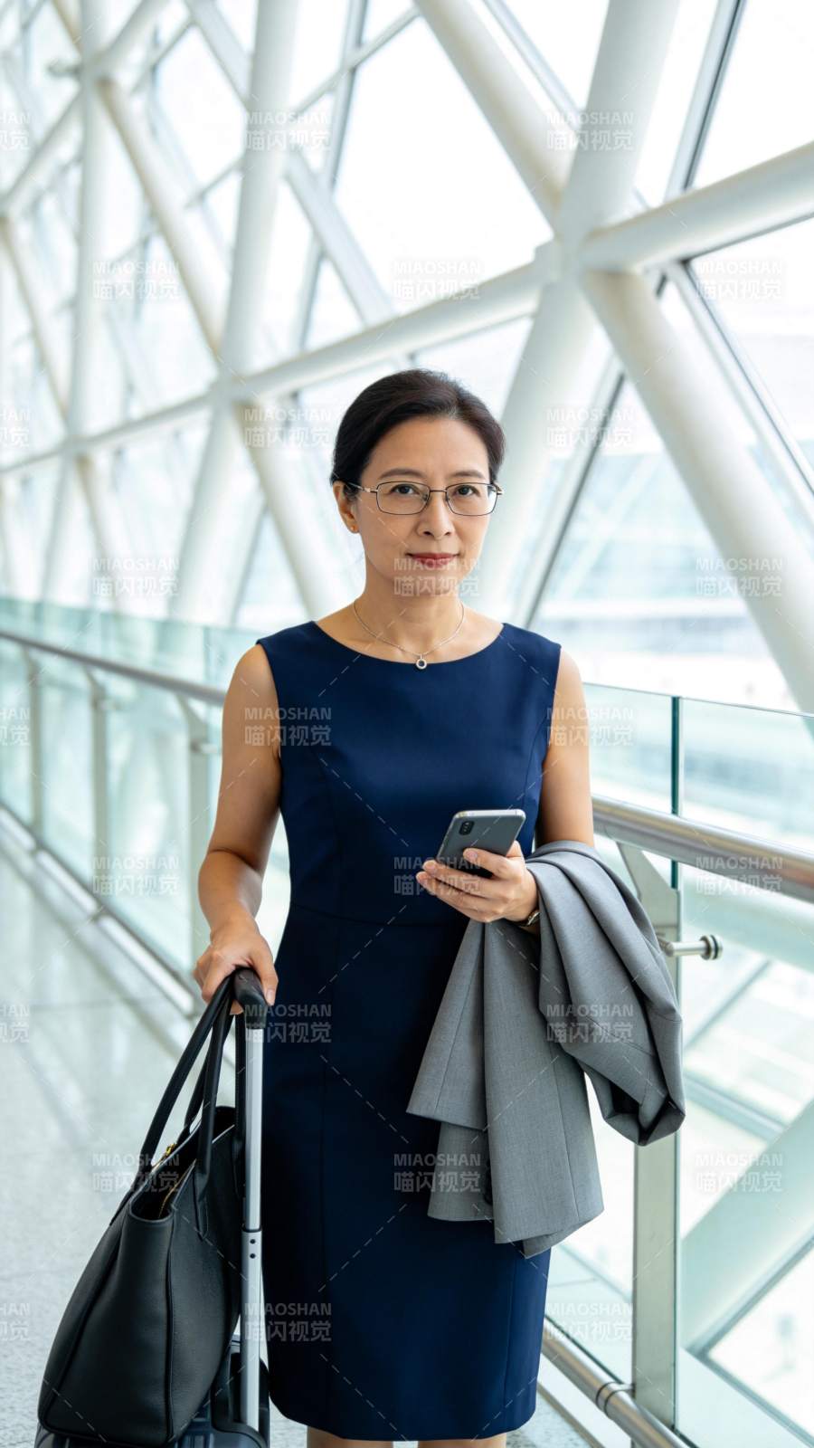 穿深蓝连衣裙女子持手机拉行李箱站立图片