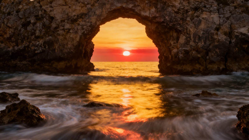 海蚀洞夕阳 金辉映浪涌图片