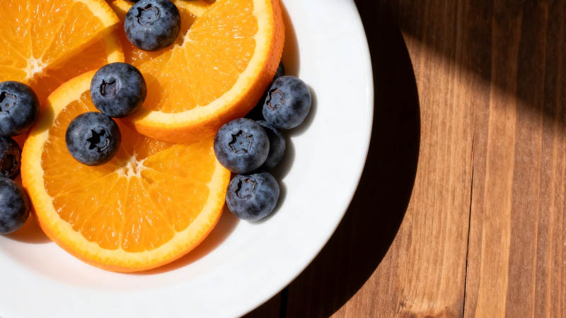 橙蓝果盘 阳光木桌旁图片