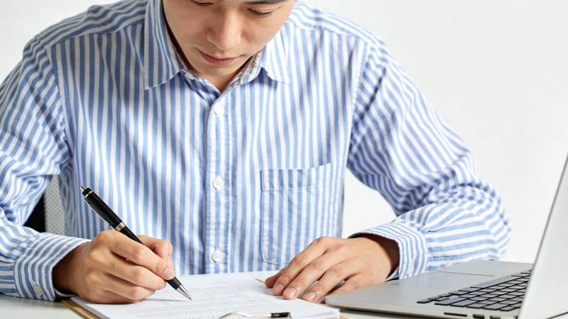 男子伏案书写 旁有笔记本电脑图片