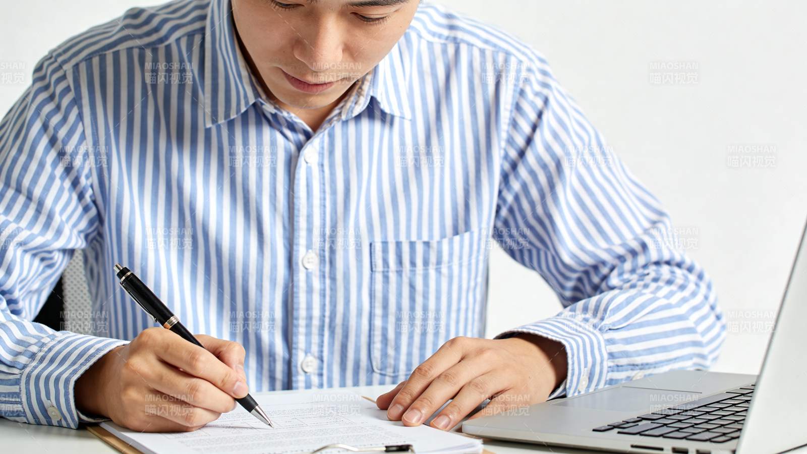 男子伏案书写 旁有笔记本电脑图片