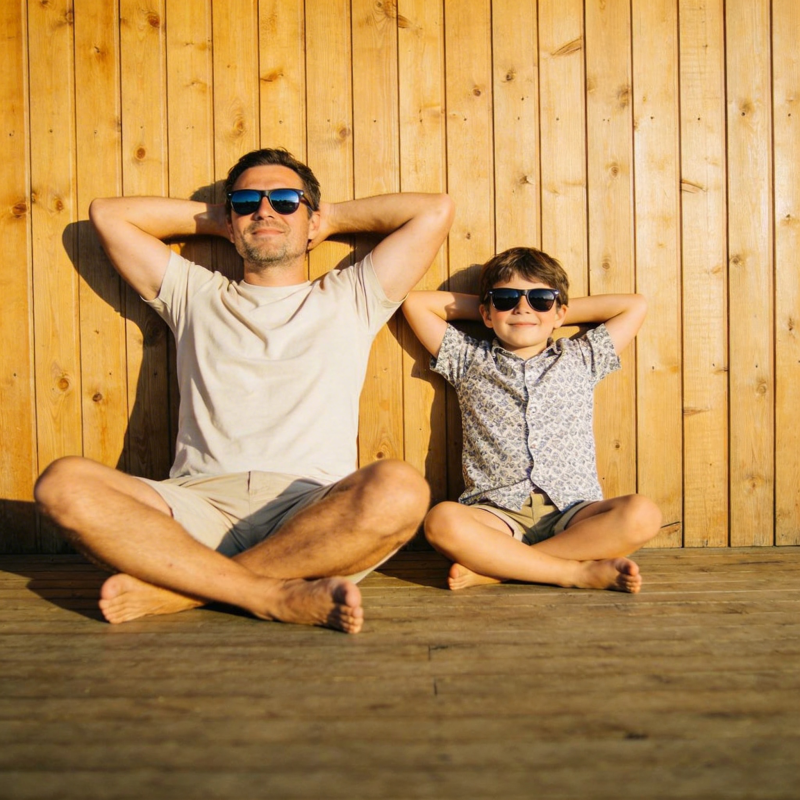 父子戴墨镜 悠闲坐木墙前图片