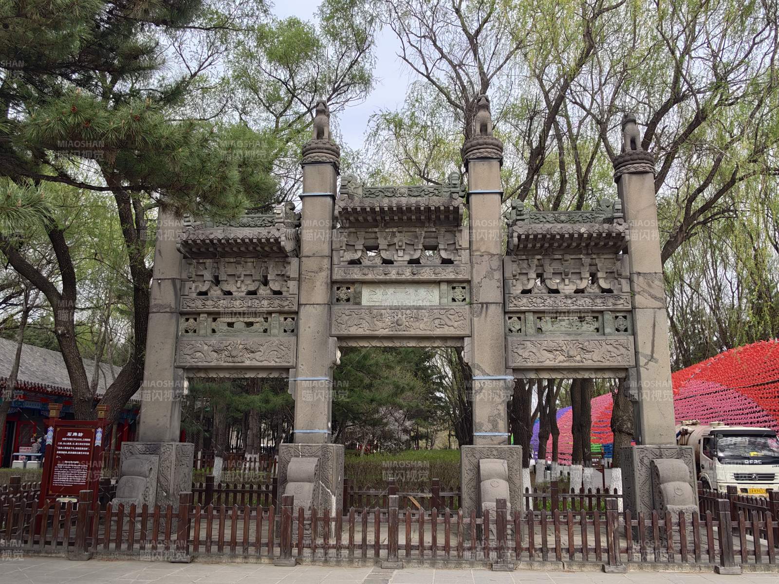 石牌坊立于绿树红墙间图片
