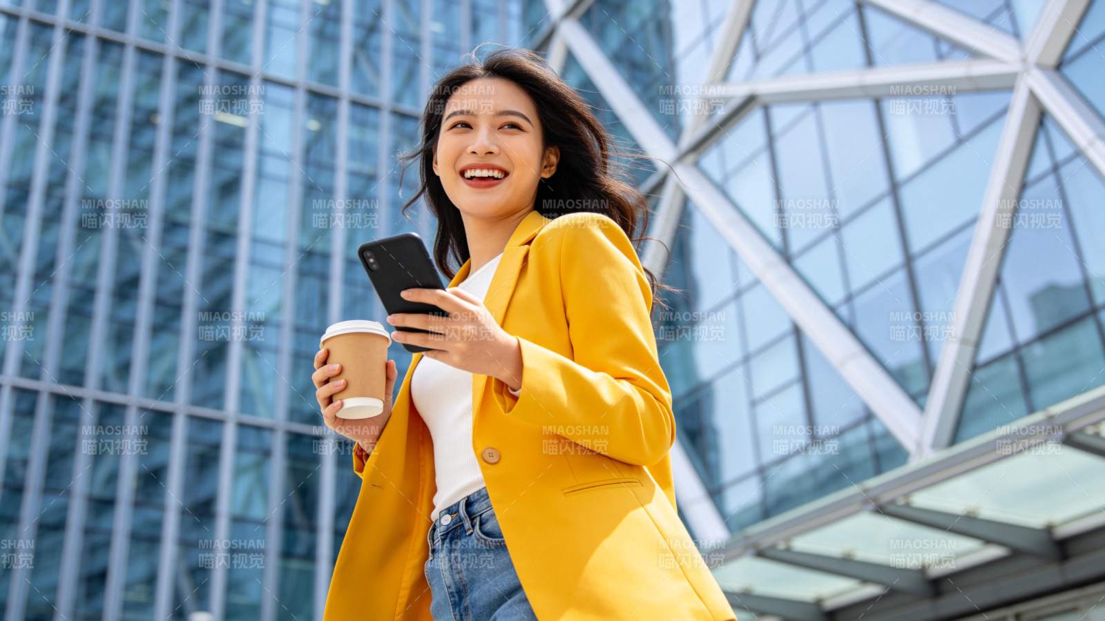 黄衣女子持手机咖啡笑立楼前图片